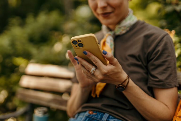 women texting on mobile phone while sitting on a bench in a park